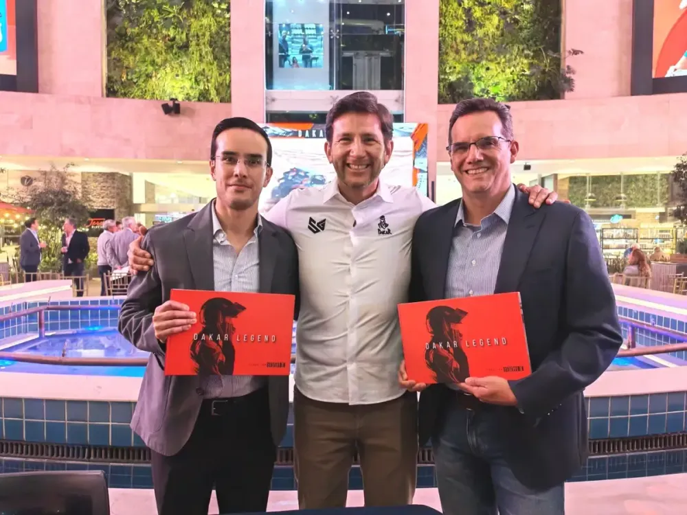 Sebastián Guayasamín junto a dos ejecutivos que sostienen el libro Dakar Legend.
